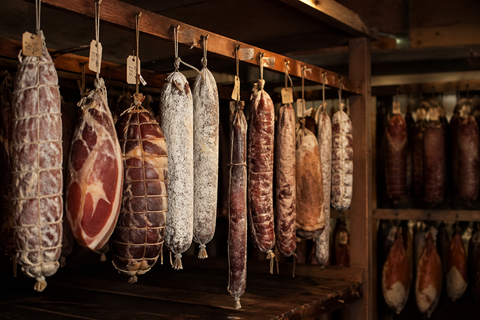 carnes curadas penduradas em ambiente controlado, estilo charcutaria tradicional, iluminação suave, atmosfera artesanal, alta qualidade