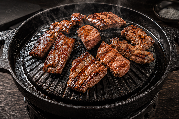 Churrasqueira gengiskan ferro fundido robusta, carnes grelhadas com crosta perfeita, vapor suave, acabamento premium, fotografia gastronômica hiper-realista, 8K.